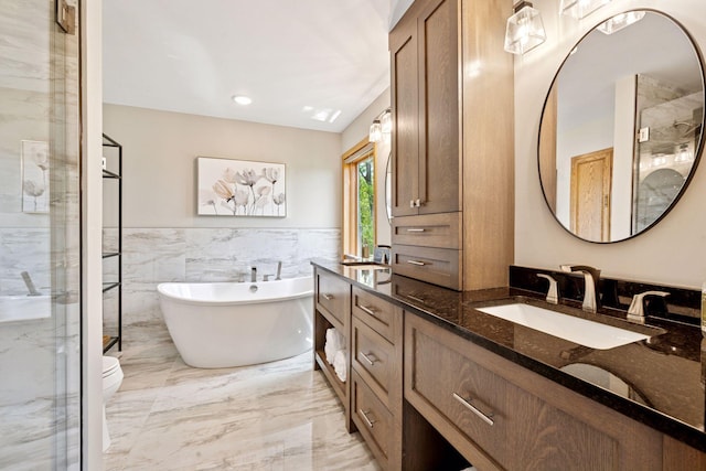 bathroom featuring marble tiled floors, tile walls, a freestanding tub, a wainscoted wall, and vanity