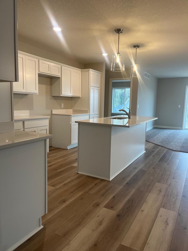 1595 76th St W, Inver Grove Heights, MN 55077 - kitchen with white cabinets, an island with sink, wood finished floors, a textured ceiling, and a sink