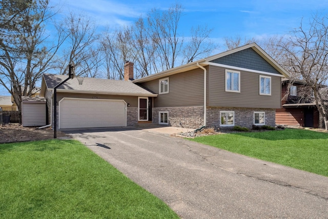 tri-level home with driveway, stone siding, a chimney, an attached garage, and a front yard