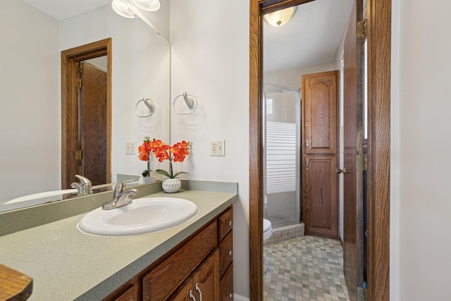 bathroom with toilet, vanity, a textured ceiling, and a stall shower