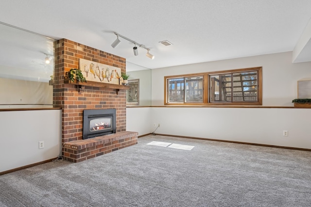 unfurnished living room with track lighting, carpet floors, a brick fireplace, and visible vents