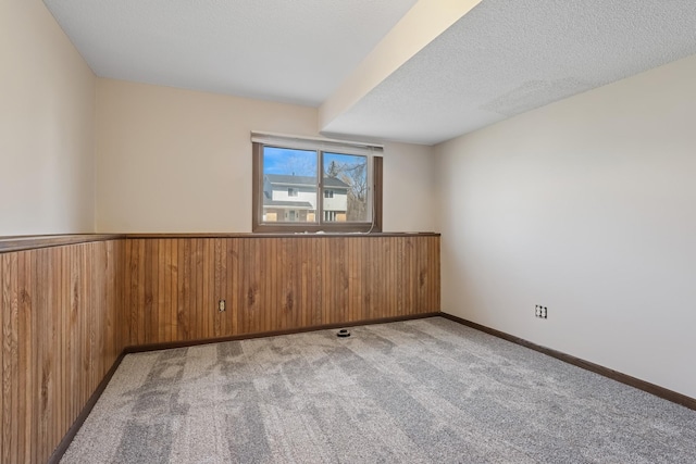 carpeted spare room with a wainscoted wall, wood walls, and a textured ceiling