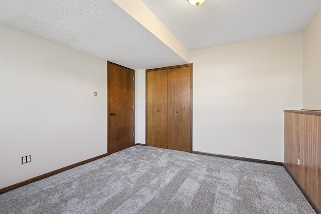 unfurnished bedroom with a textured ceiling, baseboards, carpet floors, and a closet