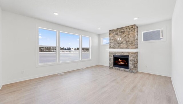 unfurnished living room with baseboards, a stone fireplace, and light wood finished floors