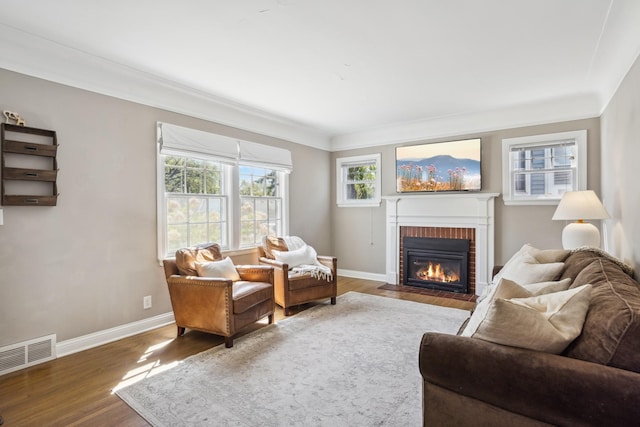 living area with a brick fireplace, wood finished floors, baseboards, and ornamental molding