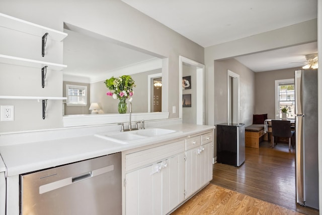 kitchen with appliances with stainless steel finishes, a sink, light countertops, light wood-style floors, and white cabinetry