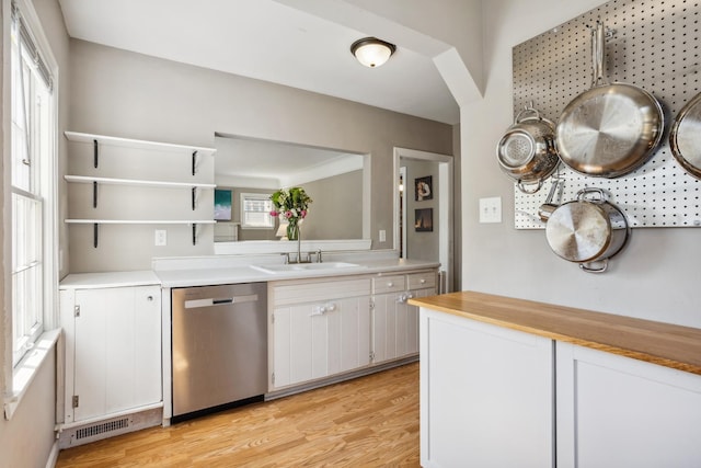 kitchen featuring stainless steel dishwasher, a sink, light wood-style flooring, and light countertops