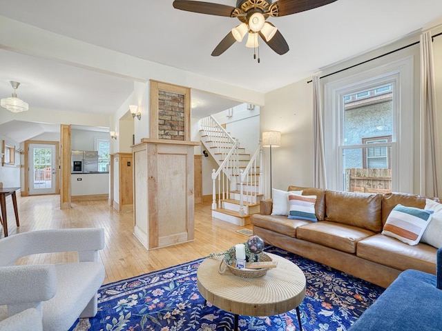 living room featuring a ceiling fan, light wood finished floors, and stairs