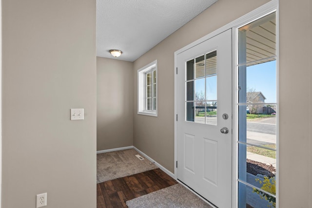 doorway to outside featuring a textured ceiling, baseboards, and dark wood-type flooring