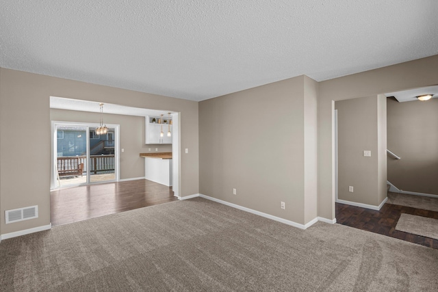 unfurnished living room featuring baseboards, dark carpet, a textured ceiling, and visible vents