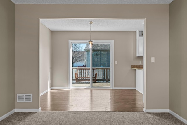 unfurnished dining area with carpet floors, a textured ceiling, baseboards, and visible vents