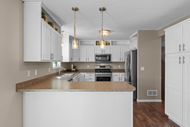 kitchen with visible vents, dark wood-style flooring, a peninsula, a sink, and stainless steel appliances