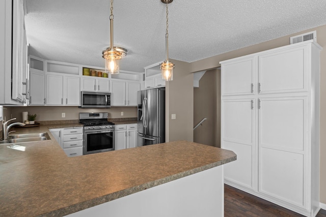 kitchen with visible vents, a sink, a peninsula, dark wood-style floors, and stainless steel appliances