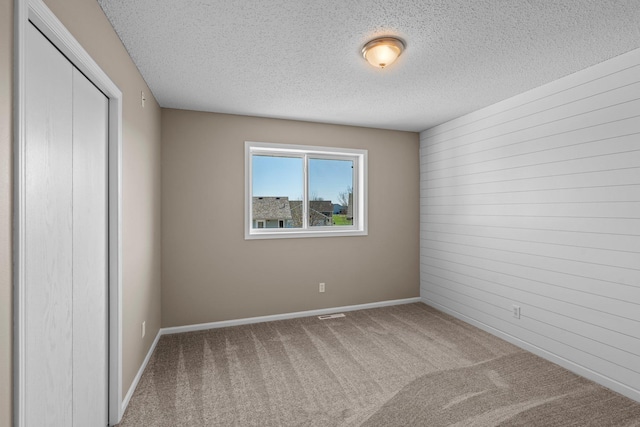 spare room featuring visible vents, wood walls, baseboards, a textured ceiling, and carpet flooring