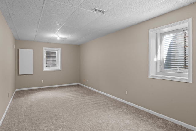 carpeted spare room featuring visible vents, baseboards, and a drop ceiling