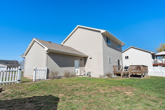 rear view of house with a lawn, a deck, and fence