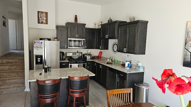 kitchen featuring light stone countertops, a kitchen bar, appliances with stainless steel finishes, a sink, and light wood finished floors
