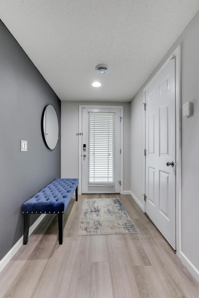 doorway to outside with light wood-style floors, visible vents, a textured ceiling, and baseboards