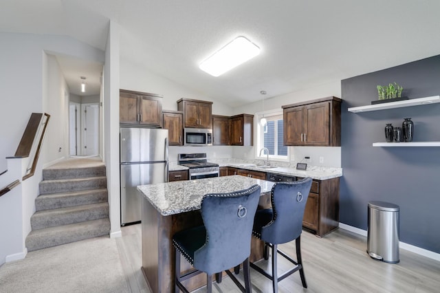kitchen featuring a sink, a center island, vaulted ceiling, baseboards, and appliances with stainless steel finishes