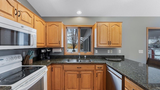 kitchen featuring white appliances, a textured ceiling, a sink, and dark stone counters