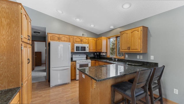kitchen with visible vents, a peninsula, white appliances, a sink, and light wood finished floors