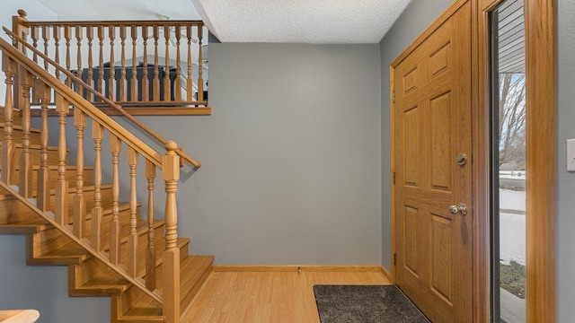 foyer featuring baseboards, a textured ceiling, wood finished floors, and a wealth of natural light