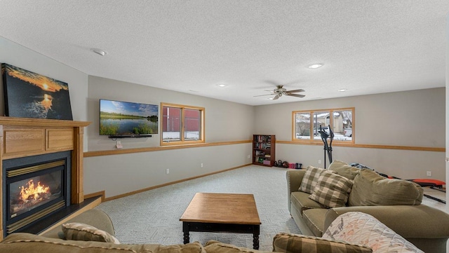carpeted living room with a ceiling fan, a textured ceiling, baseboards, a glass covered fireplace, and recessed lighting