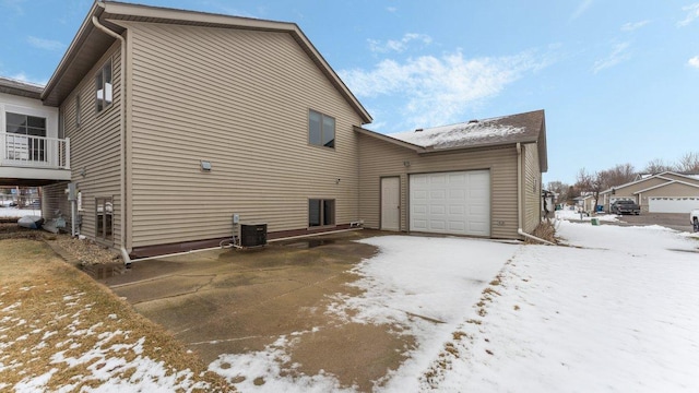 snow covered back of property featuring a garage and central AC