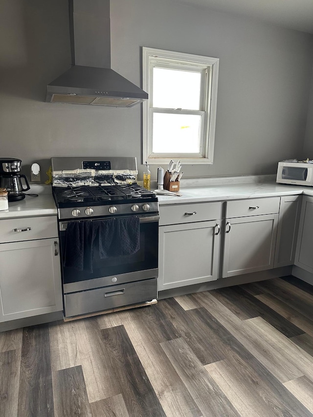 kitchen with light countertops, stainless steel gas stove, wall chimney exhaust hood, dark wood-style floors, and white microwave