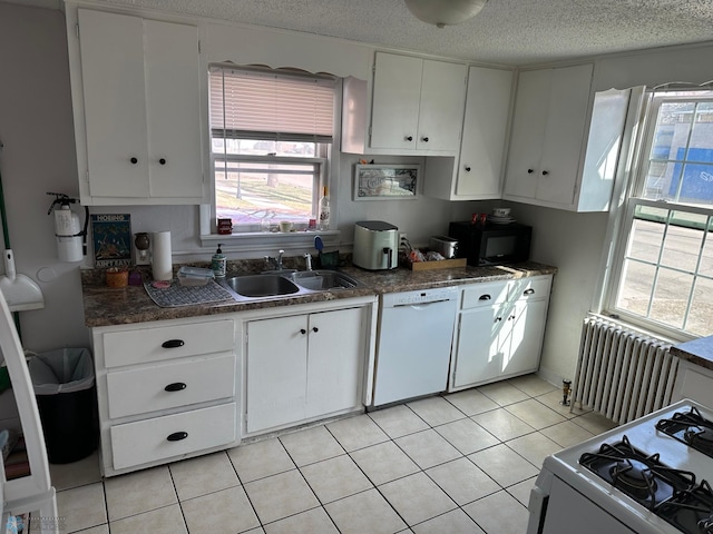kitchen with white appliances, dark countertops, radiator heating unit, white cabinets, and a sink