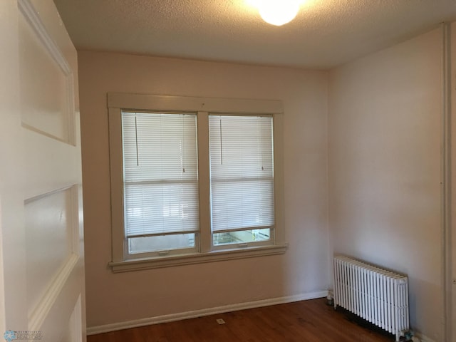 spare room with baseboards, radiator, wood finished floors, and a textured ceiling