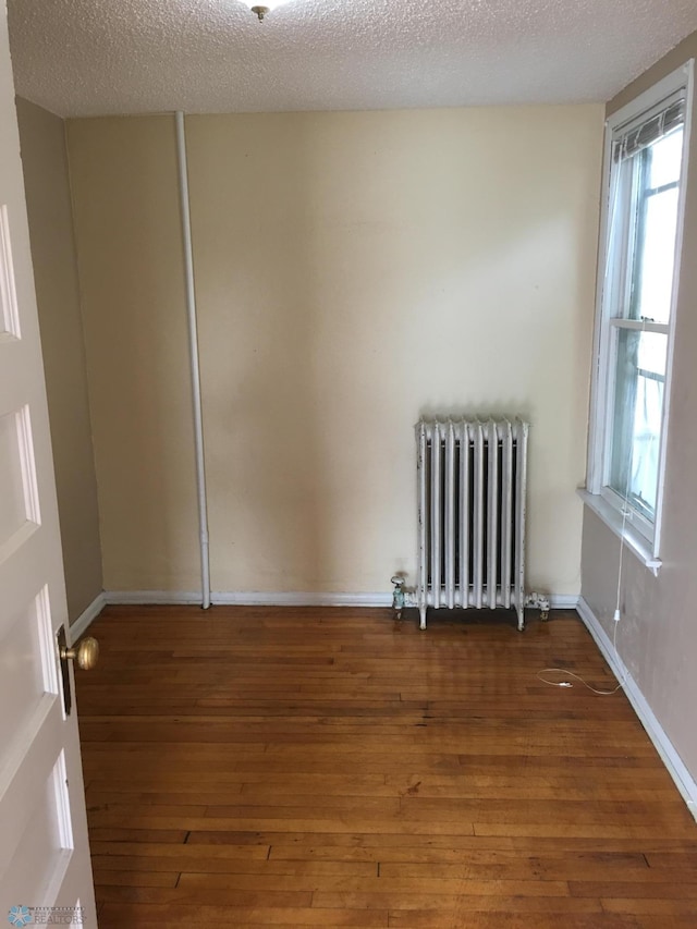 spare room featuring a wealth of natural light, wood-type flooring, and radiator