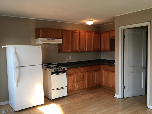 kitchen with dark countertops, white appliances, light wood-style floors, and under cabinet range hood