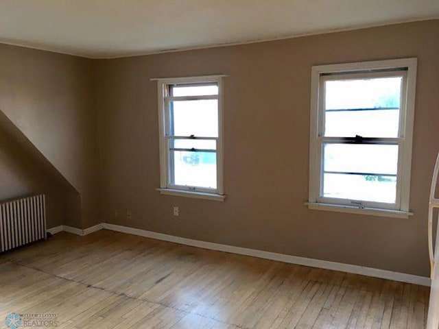 spare room featuring light wood-style floors, radiator heating unit, baseboards, and plenty of natural light