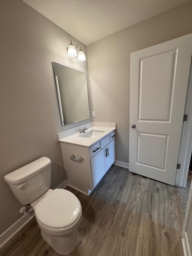 9829 89th St S, Cottage Grove, MN 55016 - bathroom with wood finished floors, toilet, vanity, a textured ceiling, and baseboards