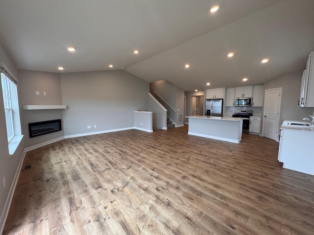 9829 89th St S, Cottage Grove, MN 55016 - unfurnished living room with a sink, wood finished floors, vaulted ceiling, stairs, and baseboards