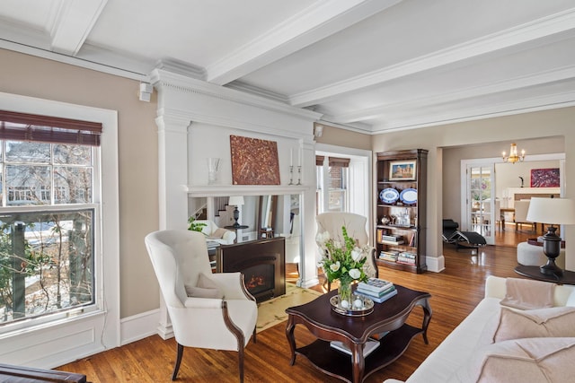 living area featuring a chandelier, a lit fireplace, beam ceiling, and wood finished floors