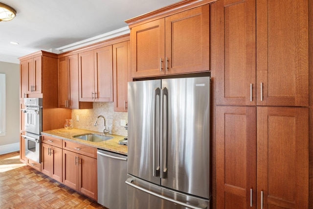 kitchen with light stone countertops, appliances with stainless steel finishes, a sink, baseboards, and backsplash