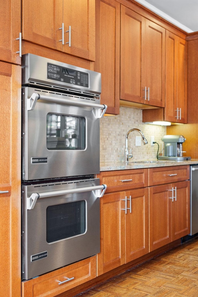 kitchen with decorative backsplash, light stone countertops, brown cabinets, a sink, and stainless steel appliances