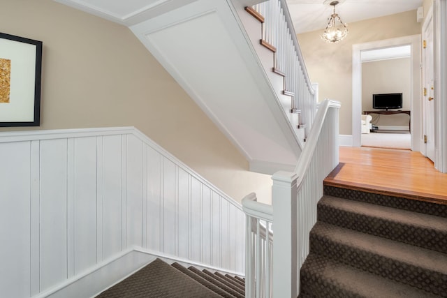 stairs featuring a wainscoted wall, a decorative wall, and a chandelier