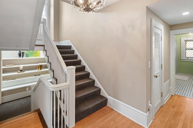 stairway featuring baseboards, a chandelier, and hardwood / wood-style floors