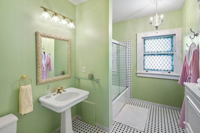 bathroom with baseboards, bath / shower combo with glass door, toilet, and a chandelier