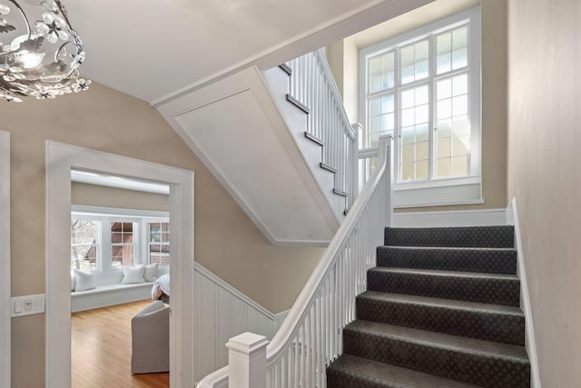 staircase featuring wainscoting, lofted ceiling, wood finished floors, and a notable chandelier