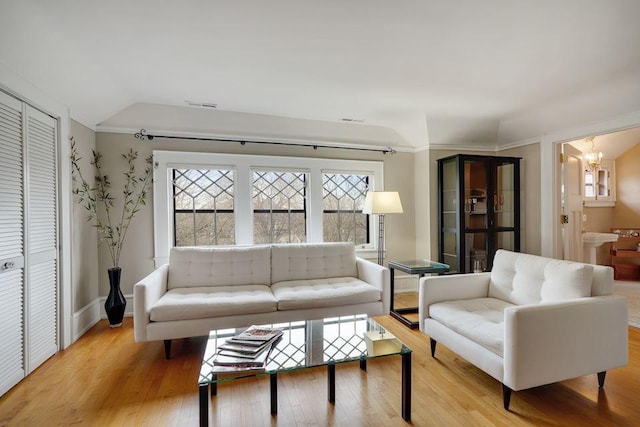 living room with wood finished floors, baseboards, a chandelier, ornamental molding, and lofted ceiling