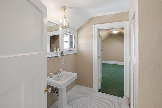 bathroom featuring an inviting chandelier, tile patterned floors, a textured wall, and vaulted ceiling