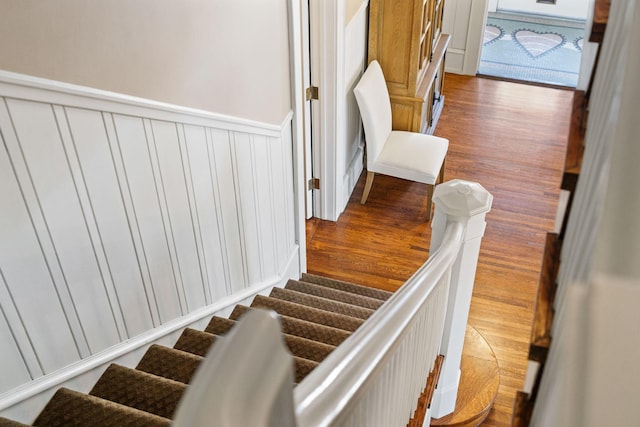 staircase with a decorative wall, wainscoting, and wood finished floors
