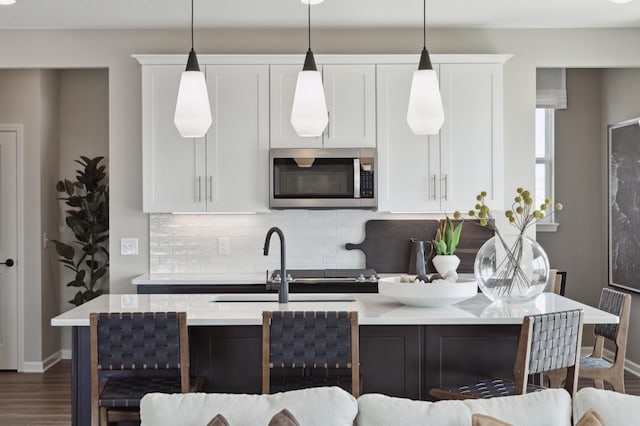 kitchen featuring stainless steel microwave, backsplash, a sink, and white cabinets