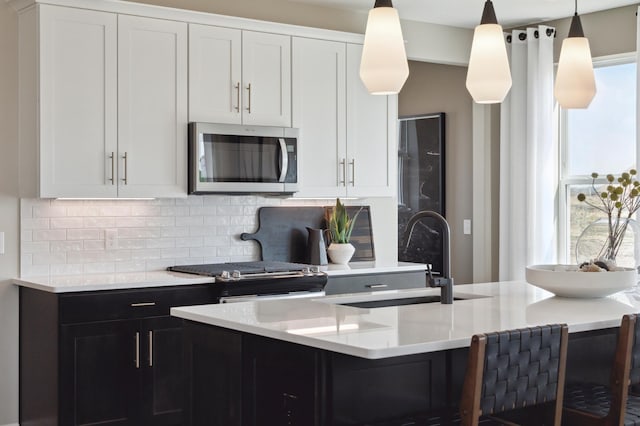 kitchen featuring appliances with stainless steel finishes, backsplash, light countertops, a sink, and white cabinets