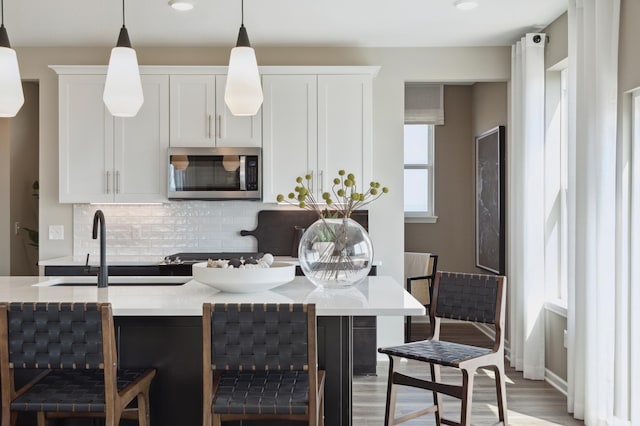 kitchen with stainless steel microwave, decorative backsplash, white cabinets, light countertops, and recessed lighting