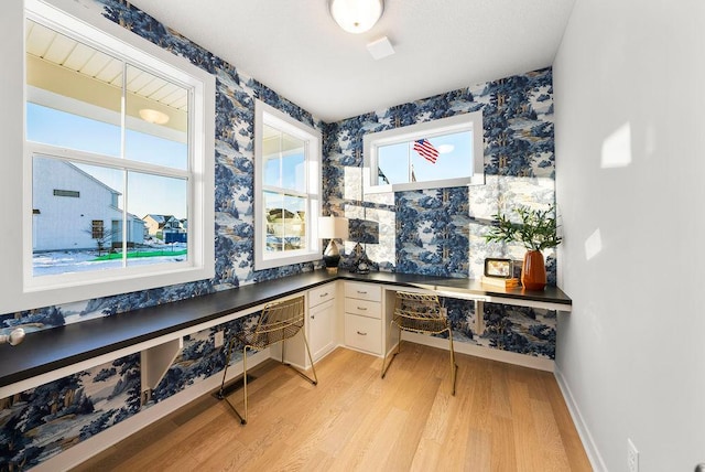 office with built in study area, wallpapered walls, baseboards, and light wood-style floors